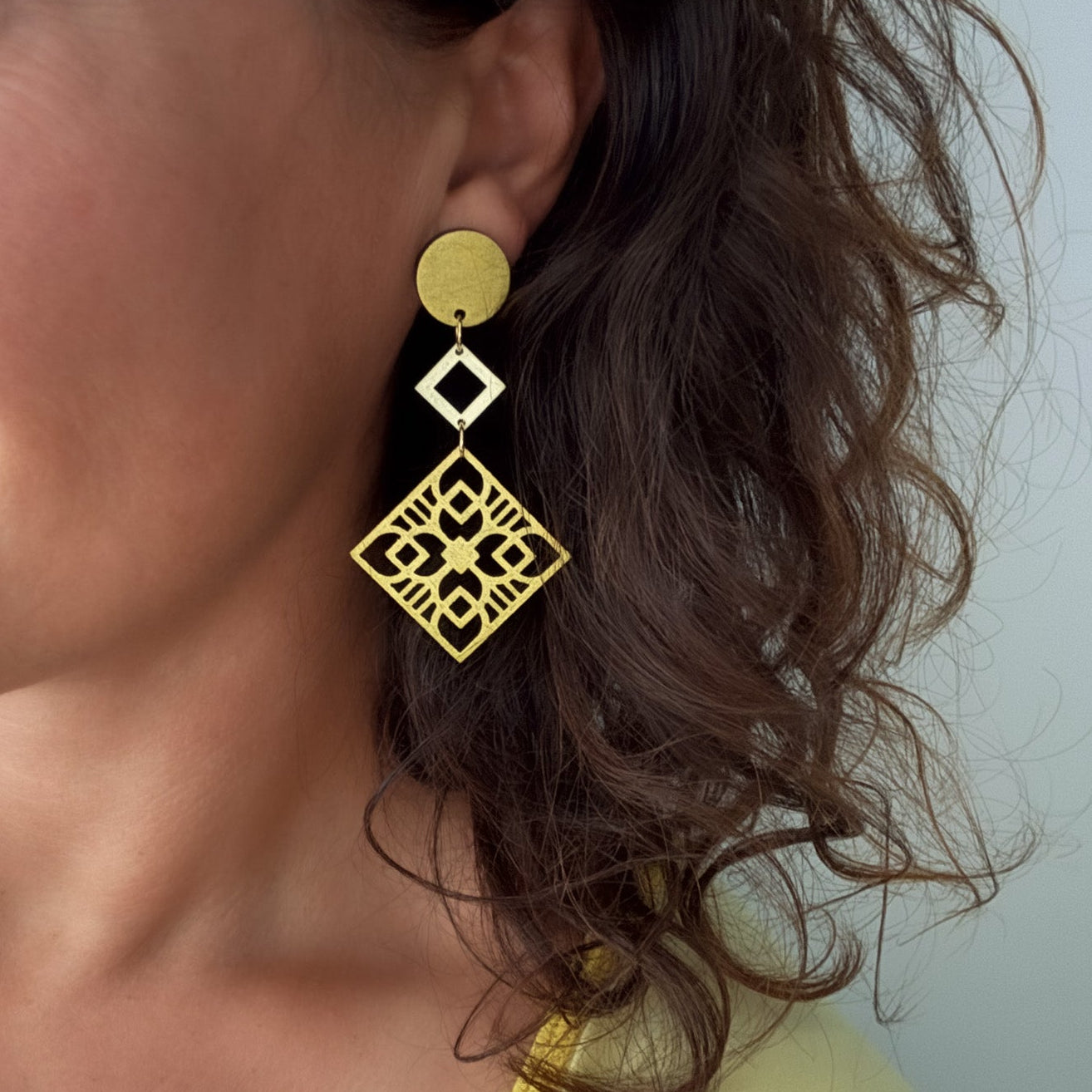 Close-up of a person wearing gold earrings with a plain background