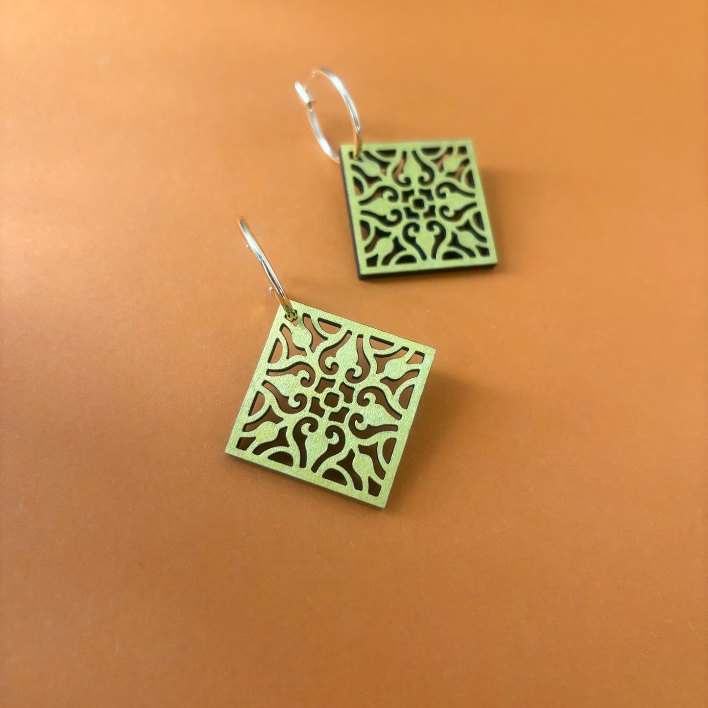 Gold square earrings with intricate patterns on an orange background