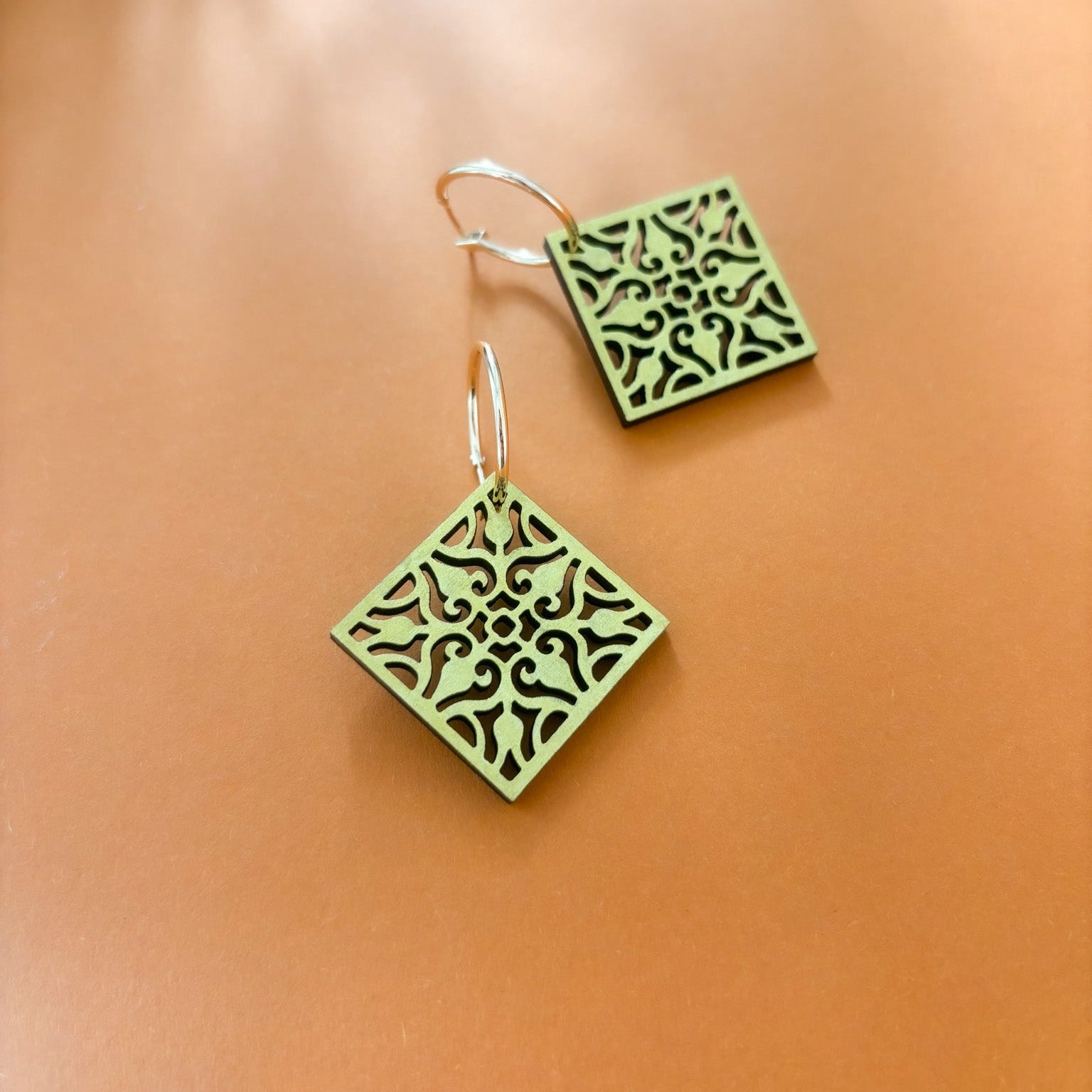 Gold square earrings with intricate patterns on a peach background