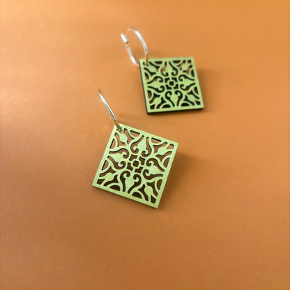 Gold square earrings with intricate patterns on an orange background